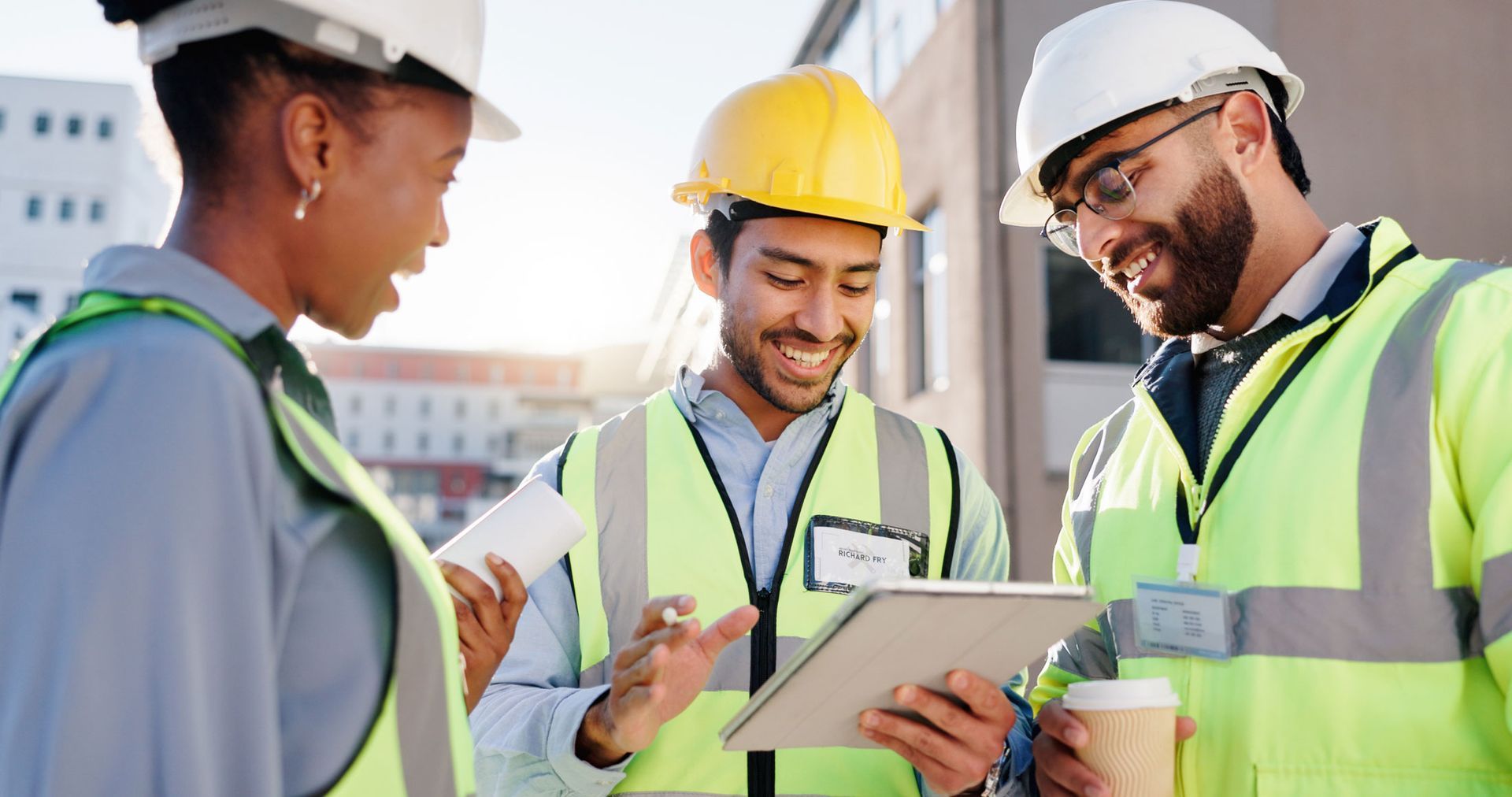 Three construction workers in hard hats reviewing plans on a tablet at a job site