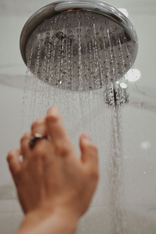 Hand under a chrome showerhead with water streaming down in a bathroom