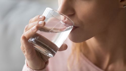 Person drinking water from a clear glass, close-up side view against a soft gray background