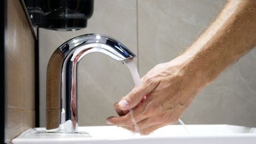 Hand washing under a chrome faucet with running water in a bathroom sink