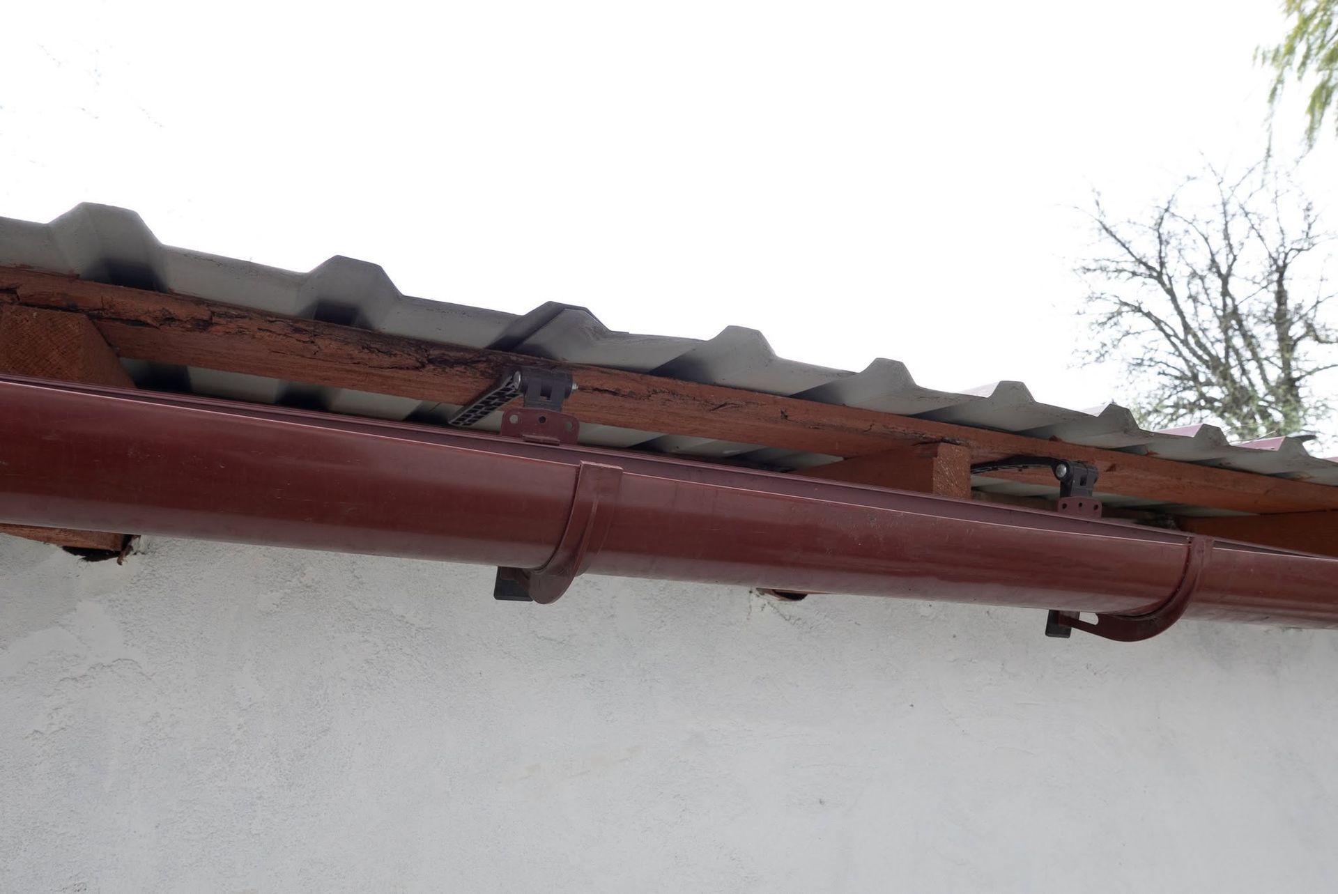 Damaged roof edge with broken tiles and a red gutter above a white wall