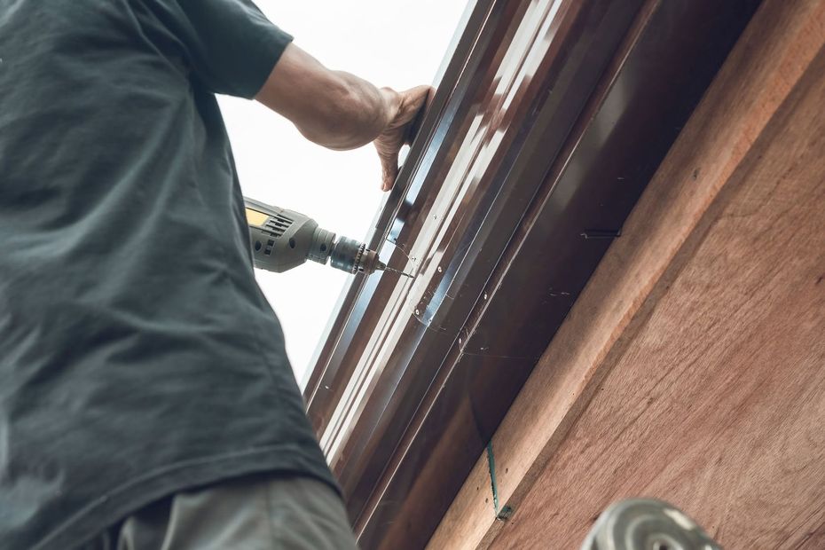 Person using a drill to work on the underside of a roof gutter on a house