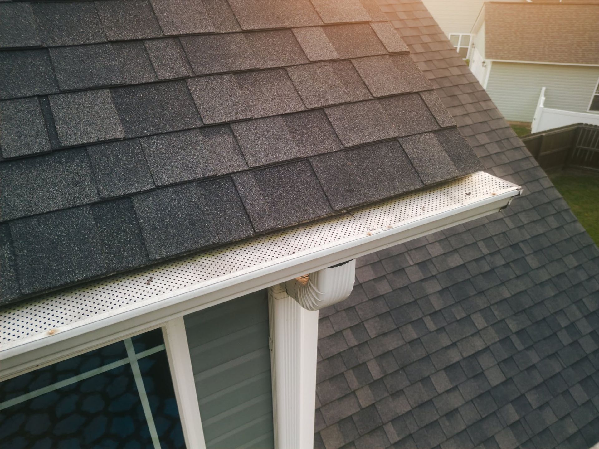 Roof shingles with a white gutter guard along the edge of a house roof.