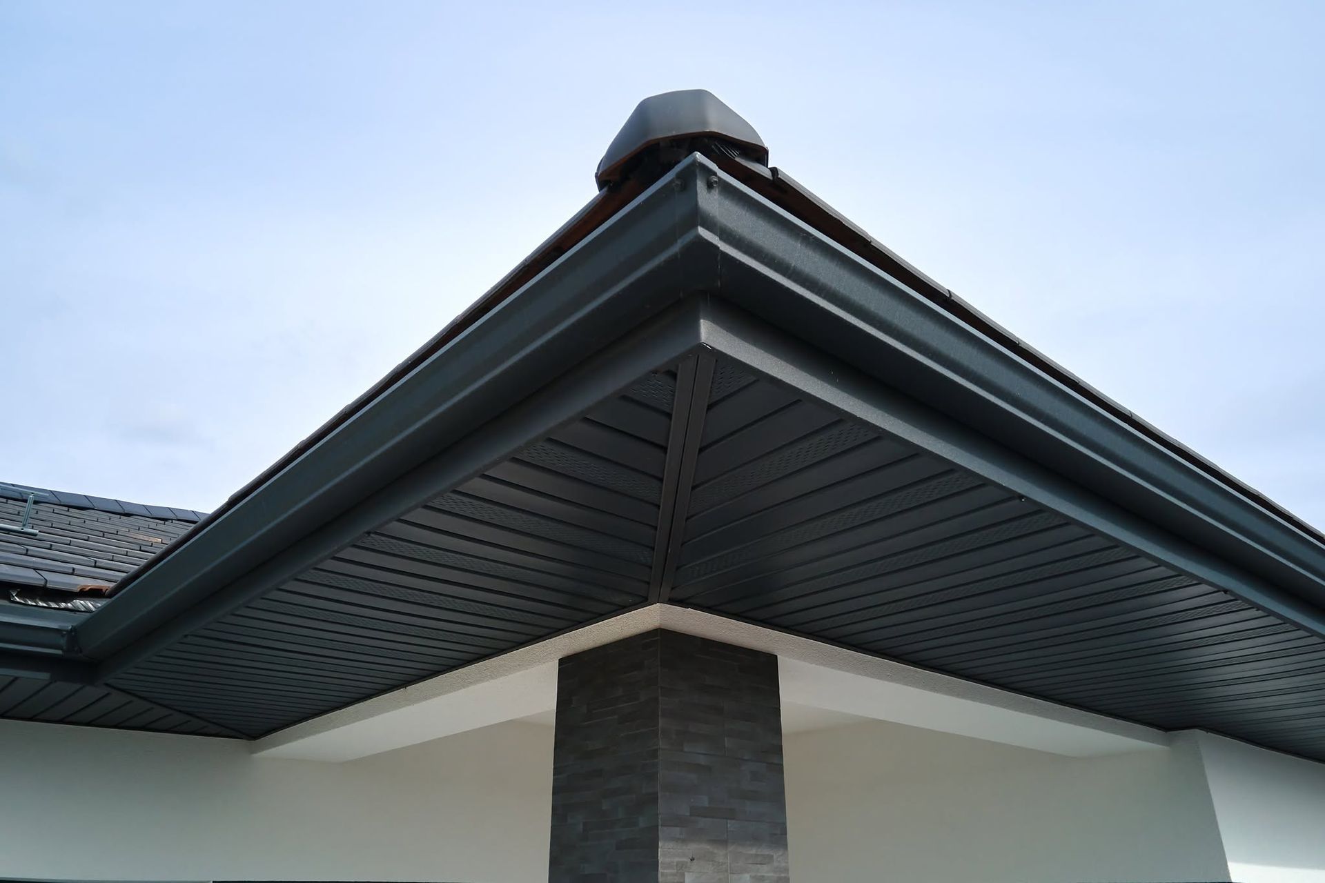 Close-up of a house roof eave with dark soffit, white trim, and stone column support