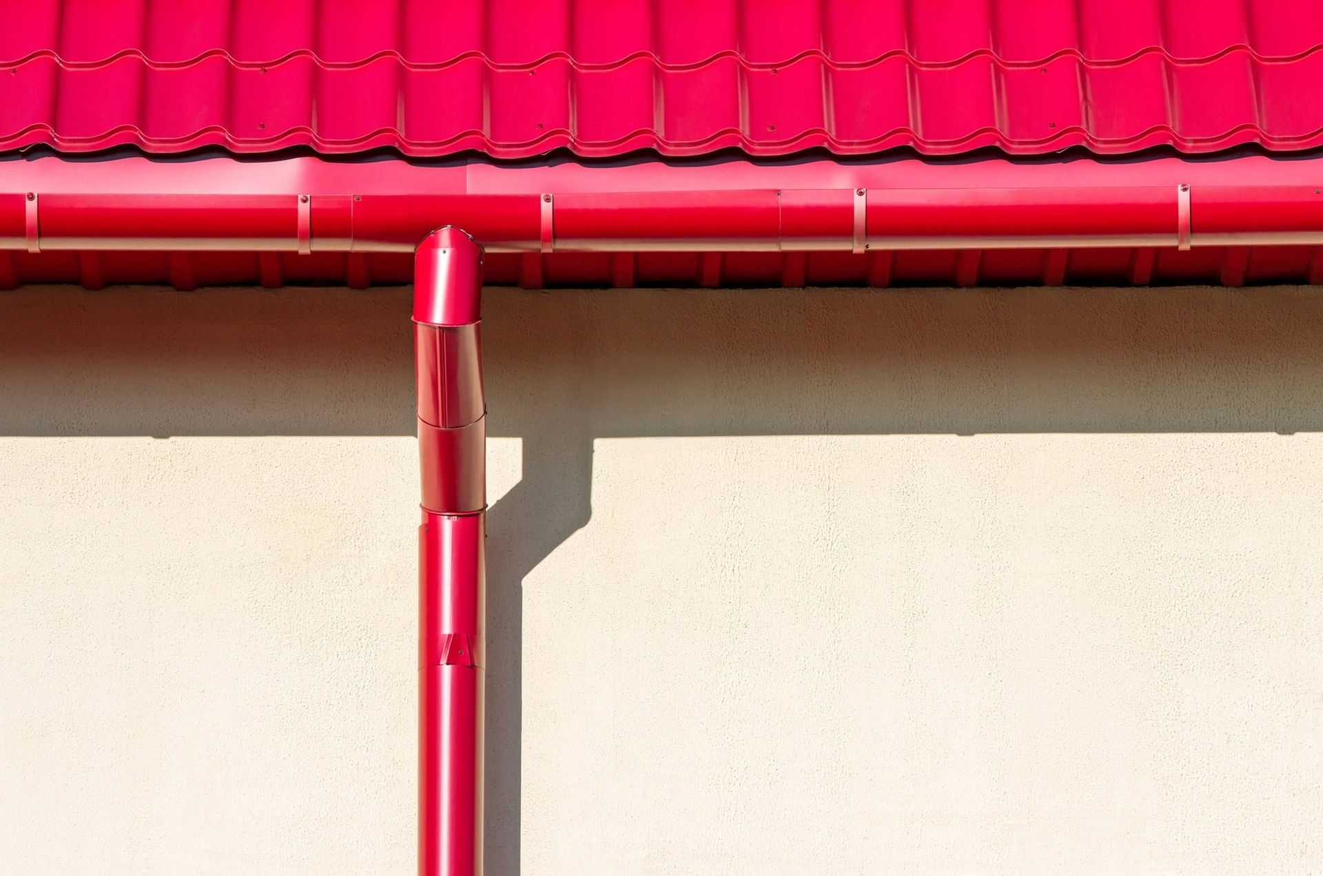 Red roof gutter and downspout against a light beige wall.
