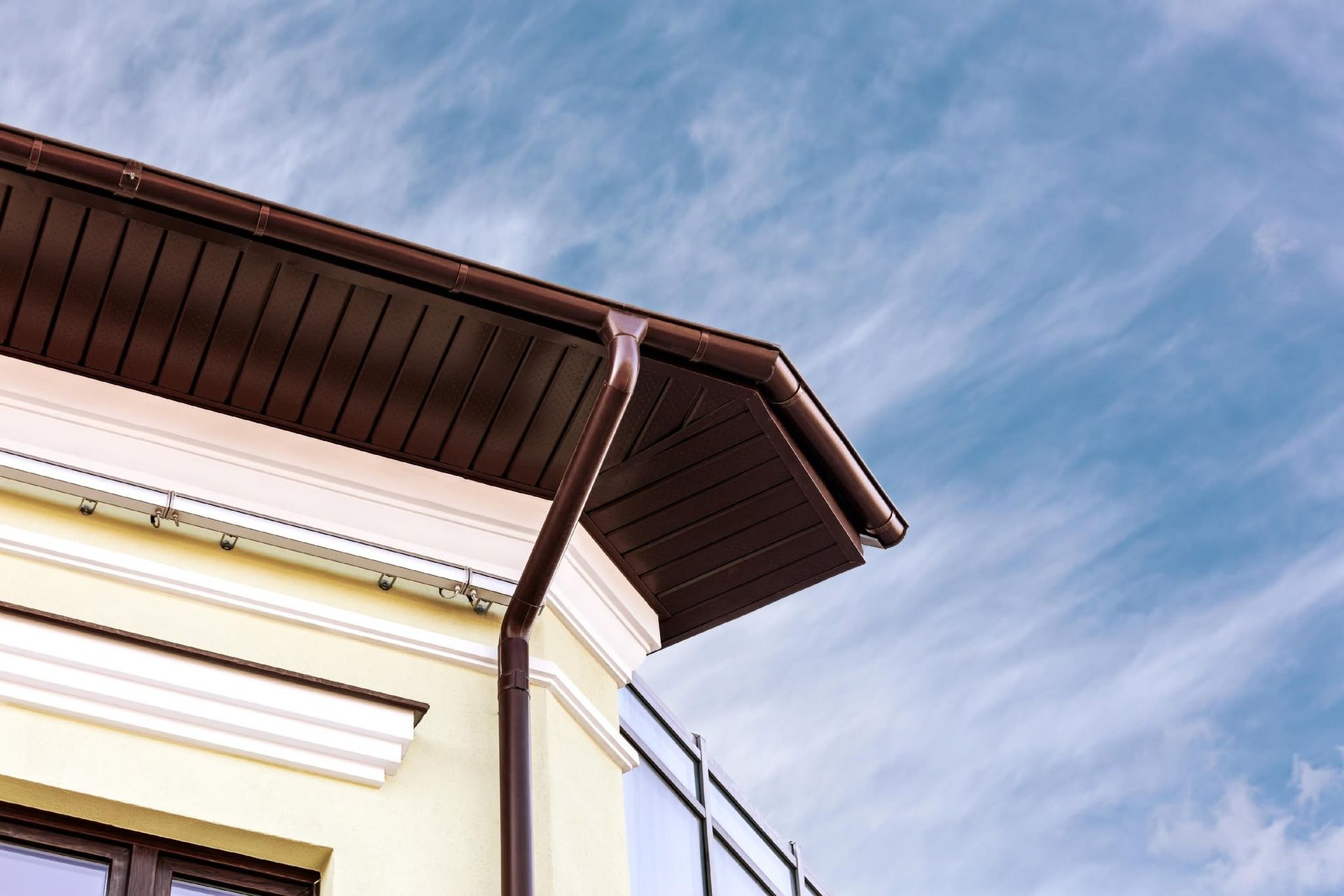 Corner of a cream building with a brown roof against a blue sky with wispy clouds