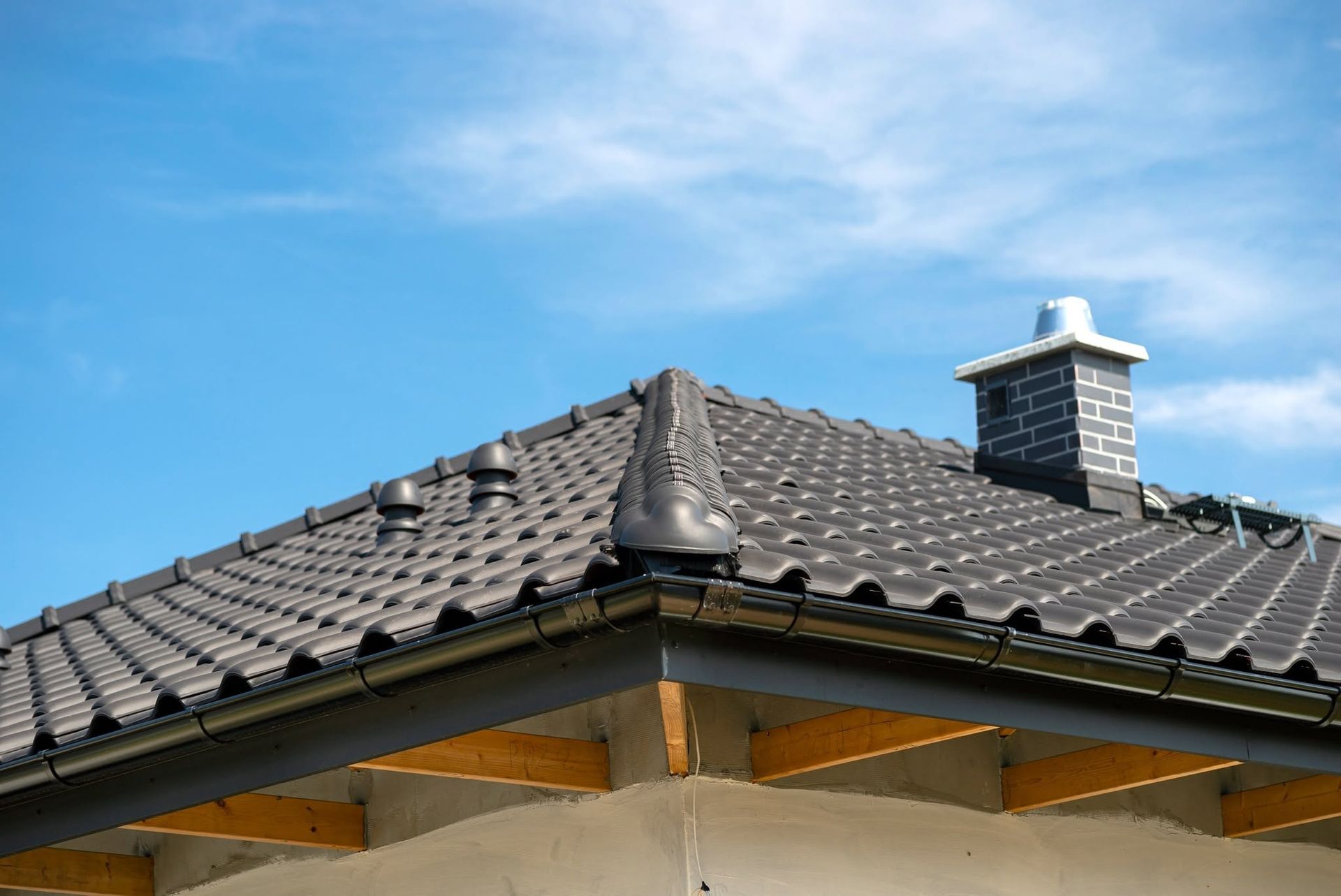 Dark gray shingled roof with a chimney under a blue sky