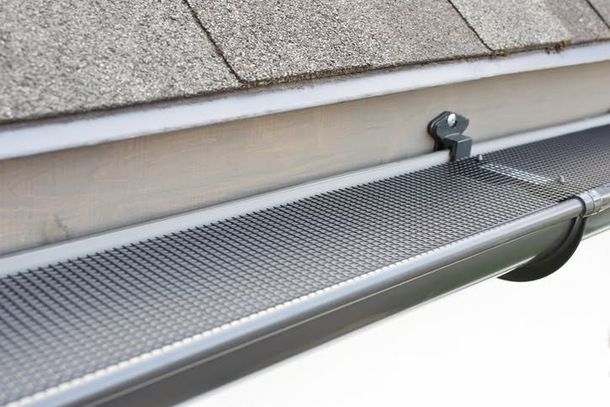 Roof gutter with mesh leaf guard beneath shingles and a metal bracket attachment