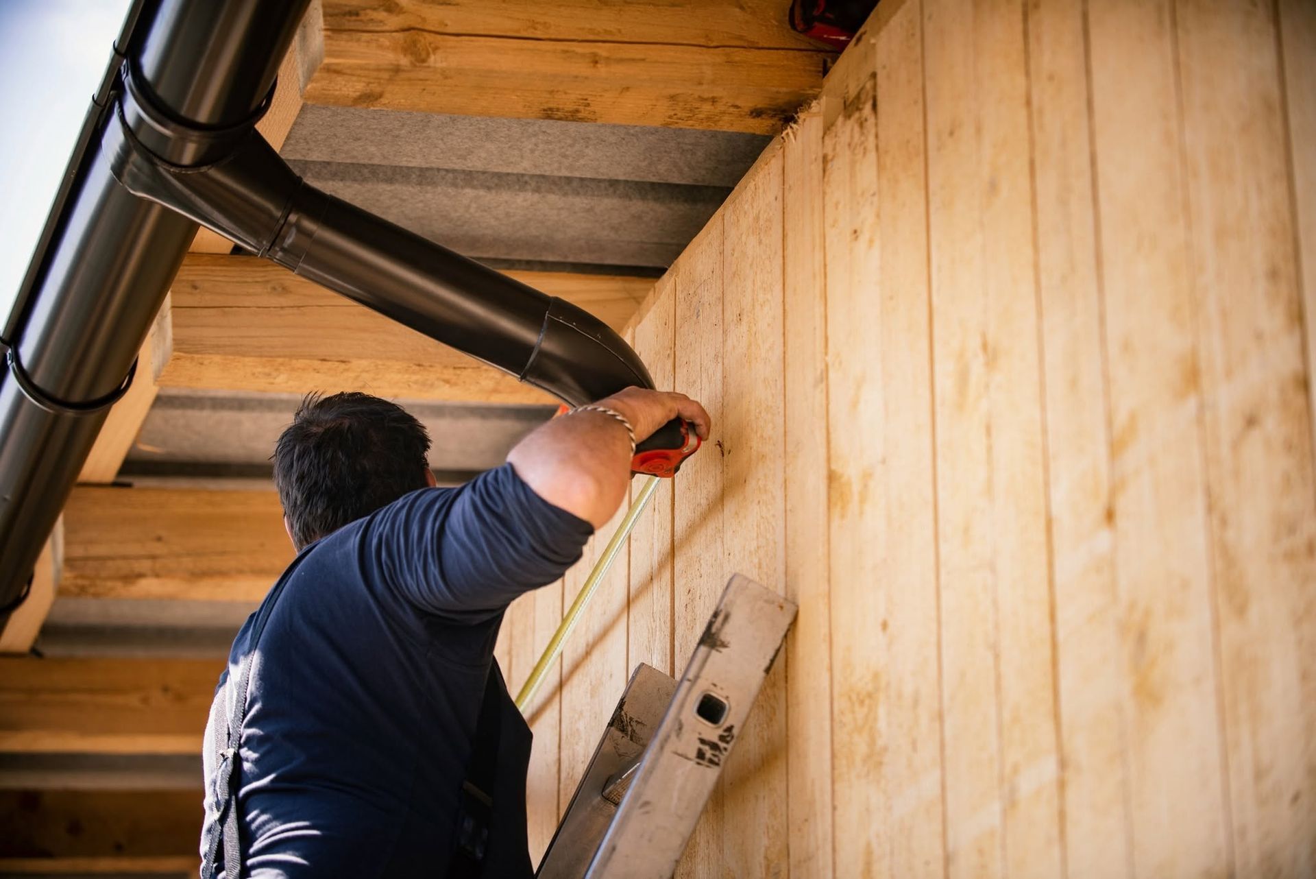 Man using a ladder to drill into a wooden wall under exposed ceiling beams