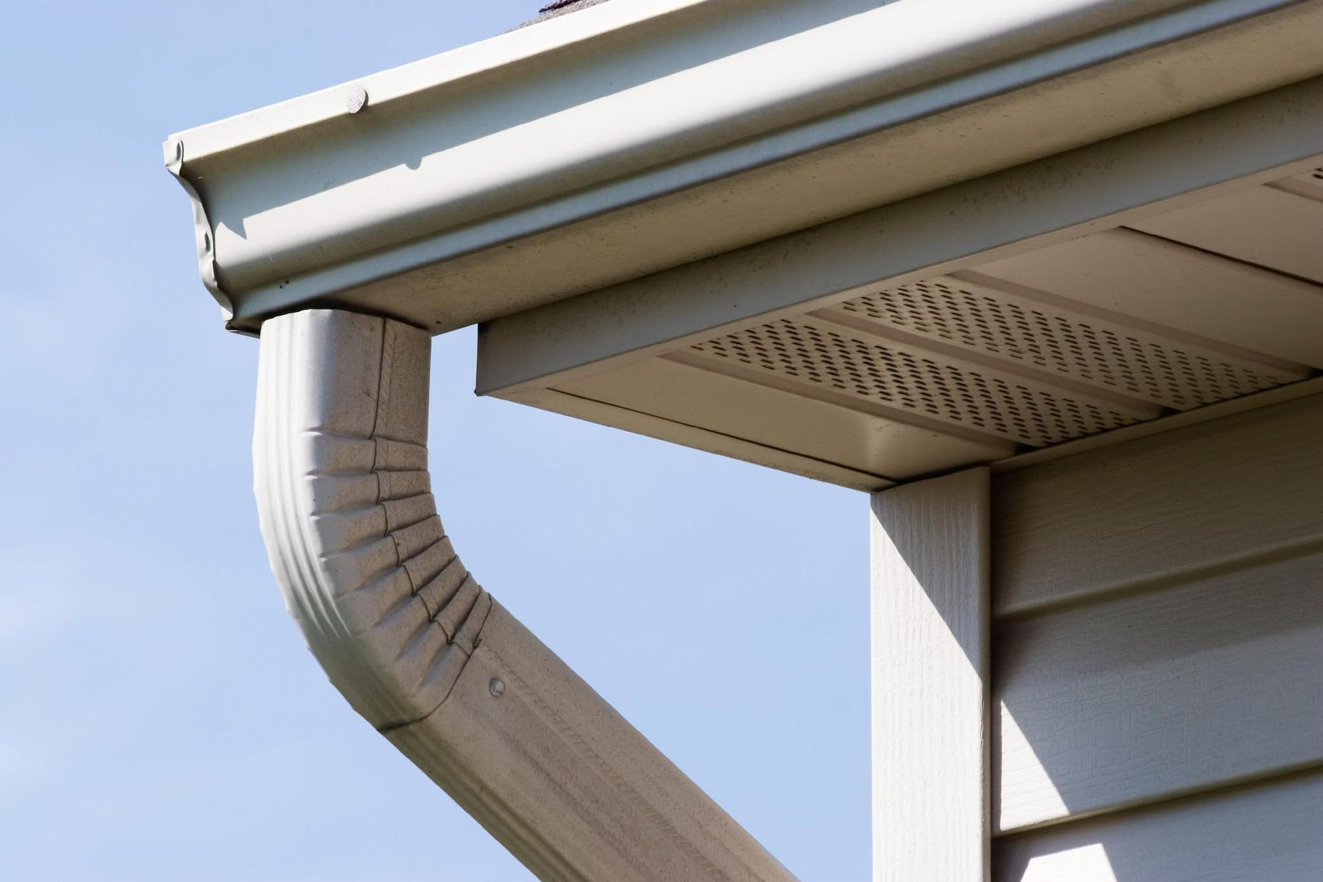 White rain gutter and downspout on a house roof against a blue sky