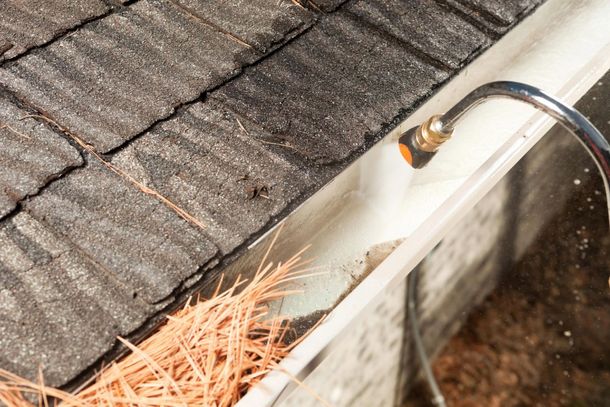 Damaged roof gutter with pine needles and debris near the edge of a shingled roof