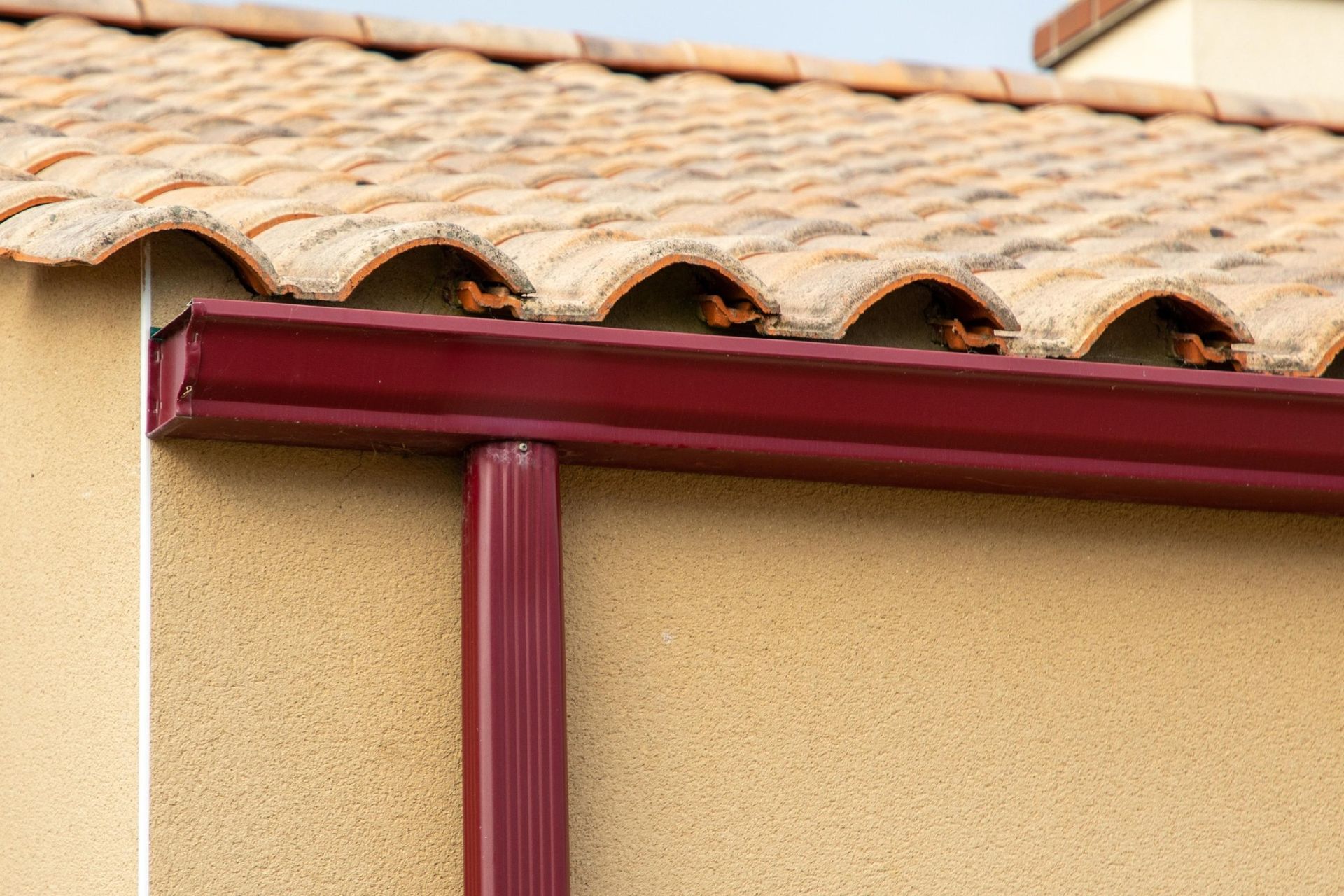 Red rain gutter under a terracotta roof edge on a beige stucco wall.