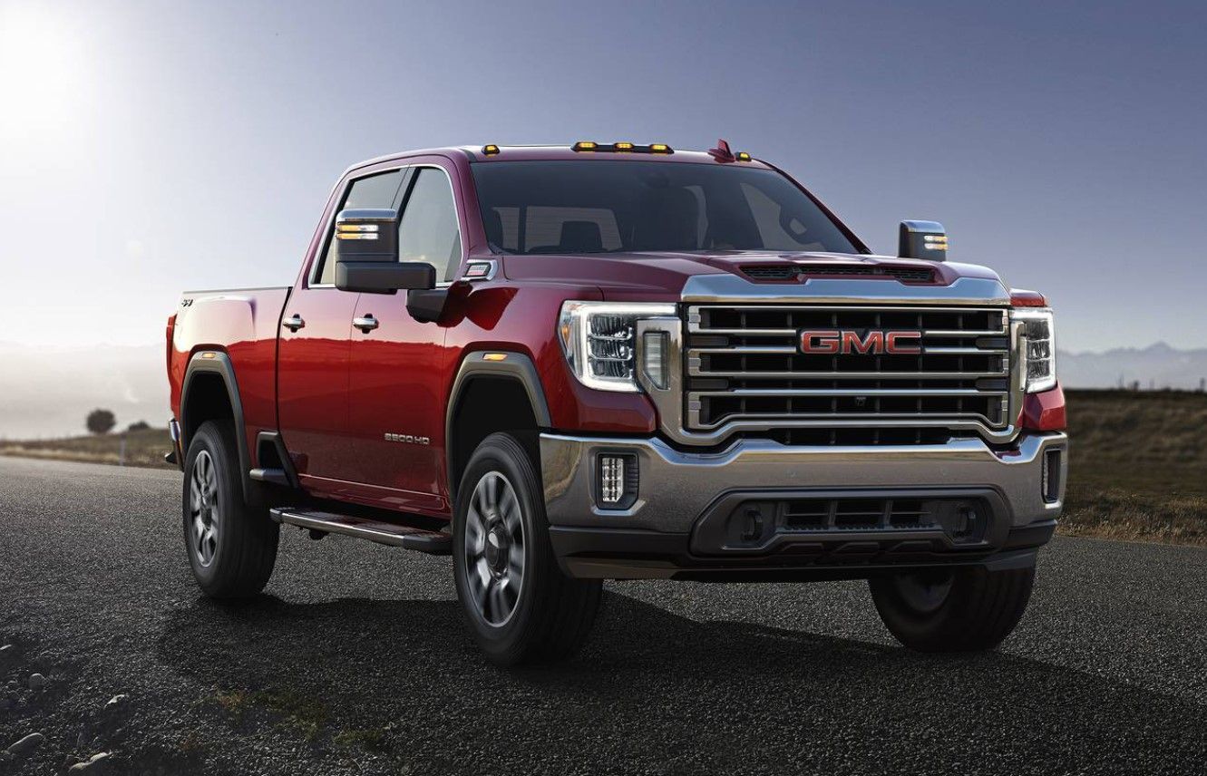 Red GMC Sierra heavy-duty truck on a road with a setting sun.