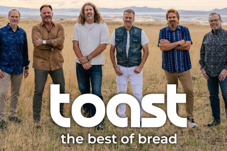 Four men, band members, smiling, posed closely together. Background of vintage signage.