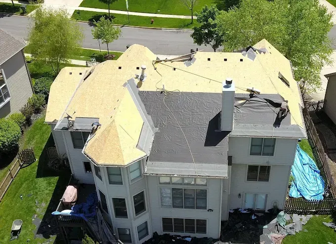 An aerial view of a large house with a new roof being installed.