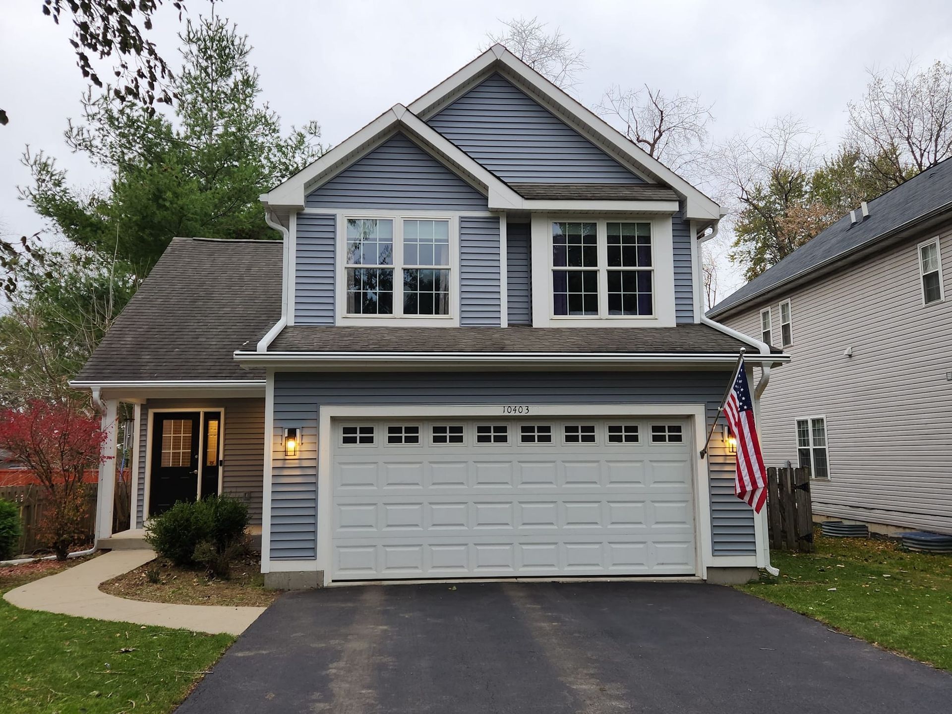 A blue house with a white garage door and an american flag in front of it