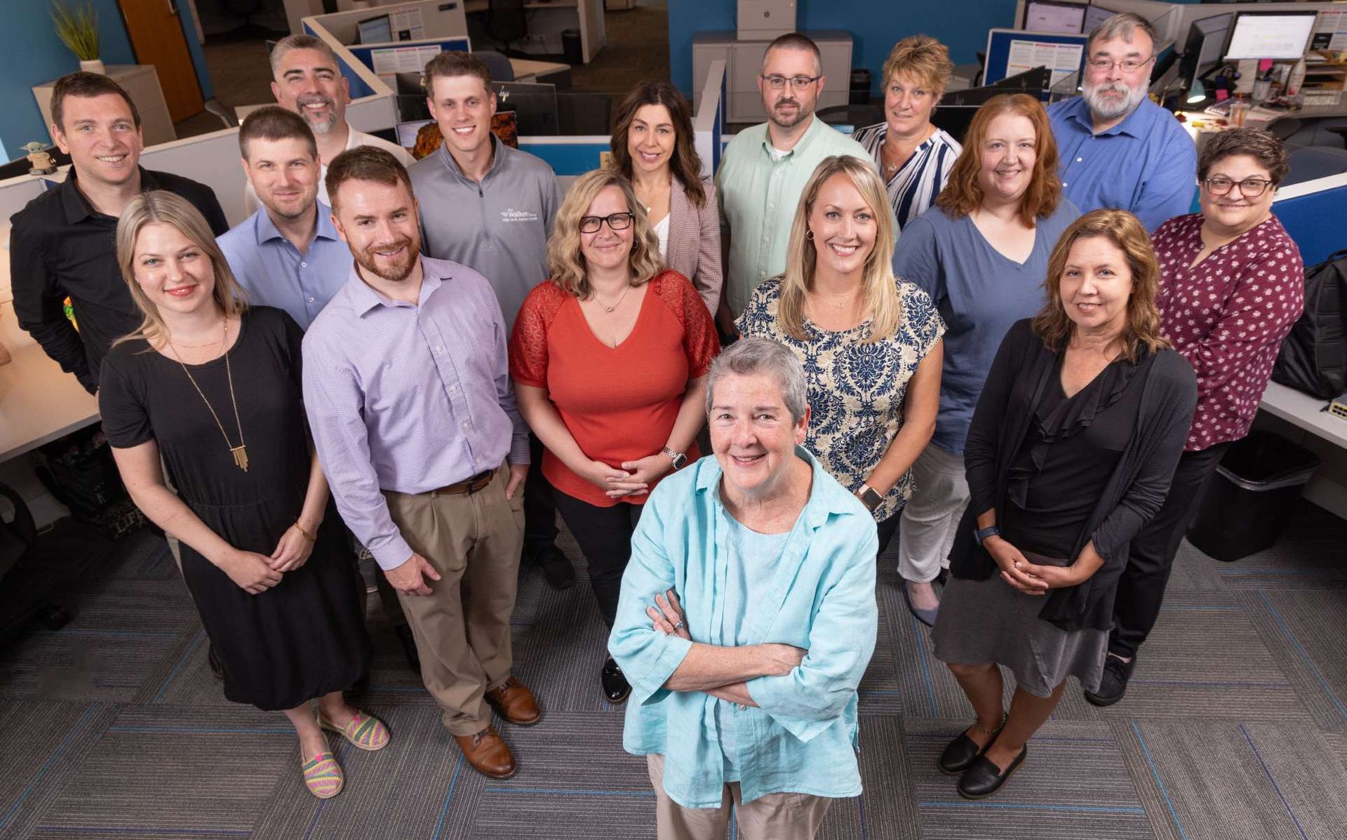 Smiling group of people with woman in front with arms crossed in light blue