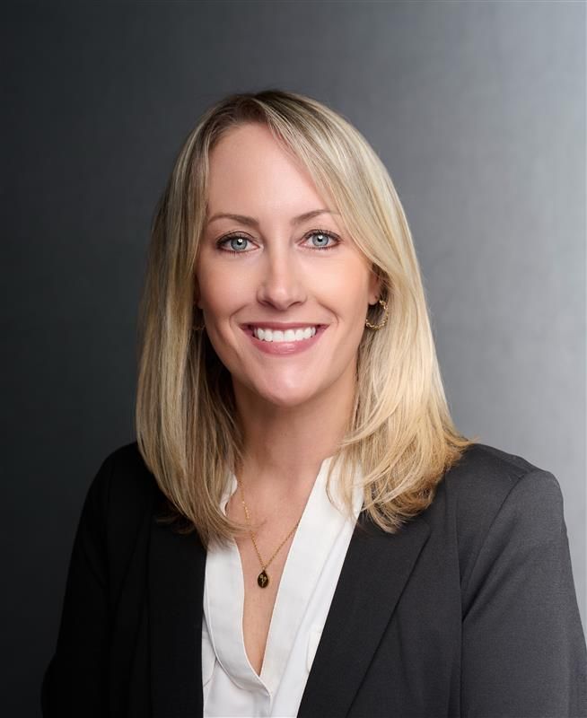 Portrait of a smiling blonde professional in a black blazer against a gray studio background
