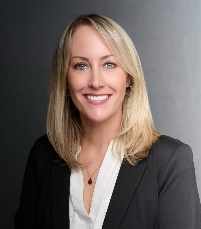 Smiling professional portrait in a gray blazer and white blouse against a dark background