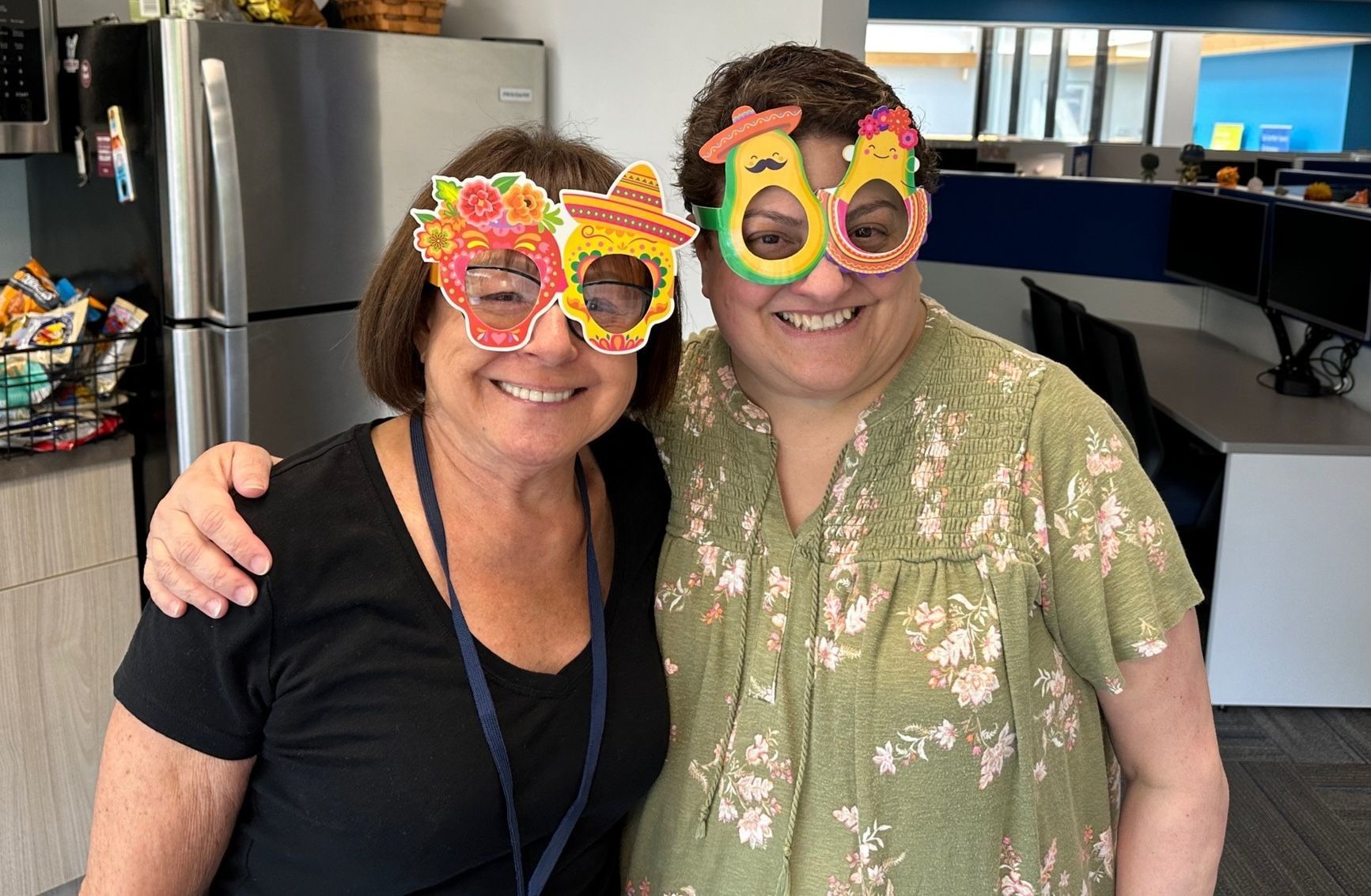 Two people smiling in novelty flower-shaped glasses in an office break room
