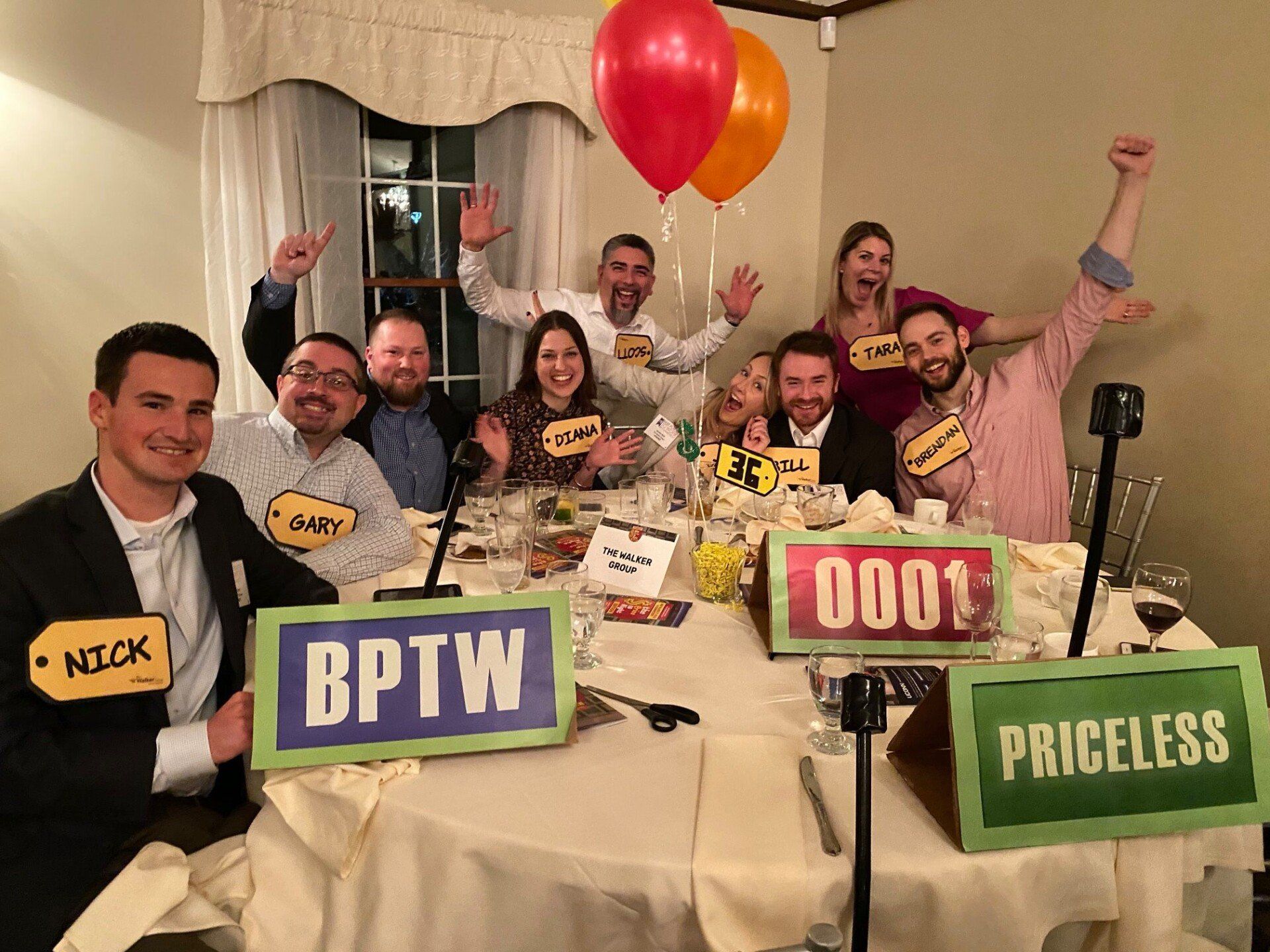 People at a banquet table holding up signs and balloons, smiling and celebrating together