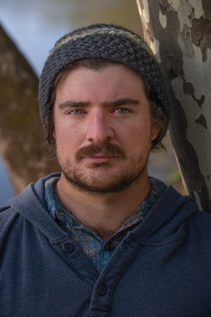 Portrait of a man in a gray knit beanie and blue jacket, standing outdoors with a serious expression