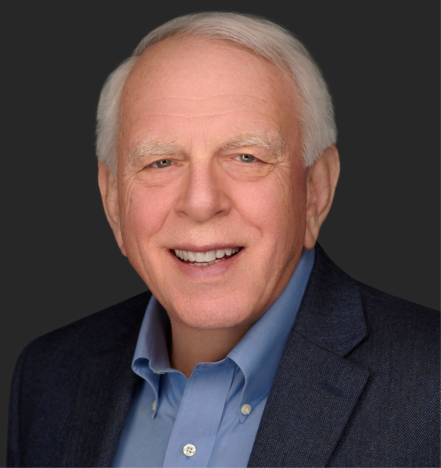 Portrait of a smiling man in a blue shirt and dark blazer against a dark background