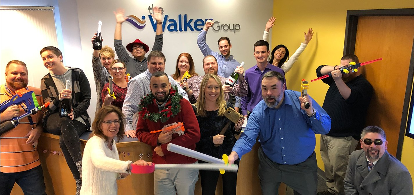 Group of coworkers posing indoors with raised arms and playful props beside a WalkMe sign