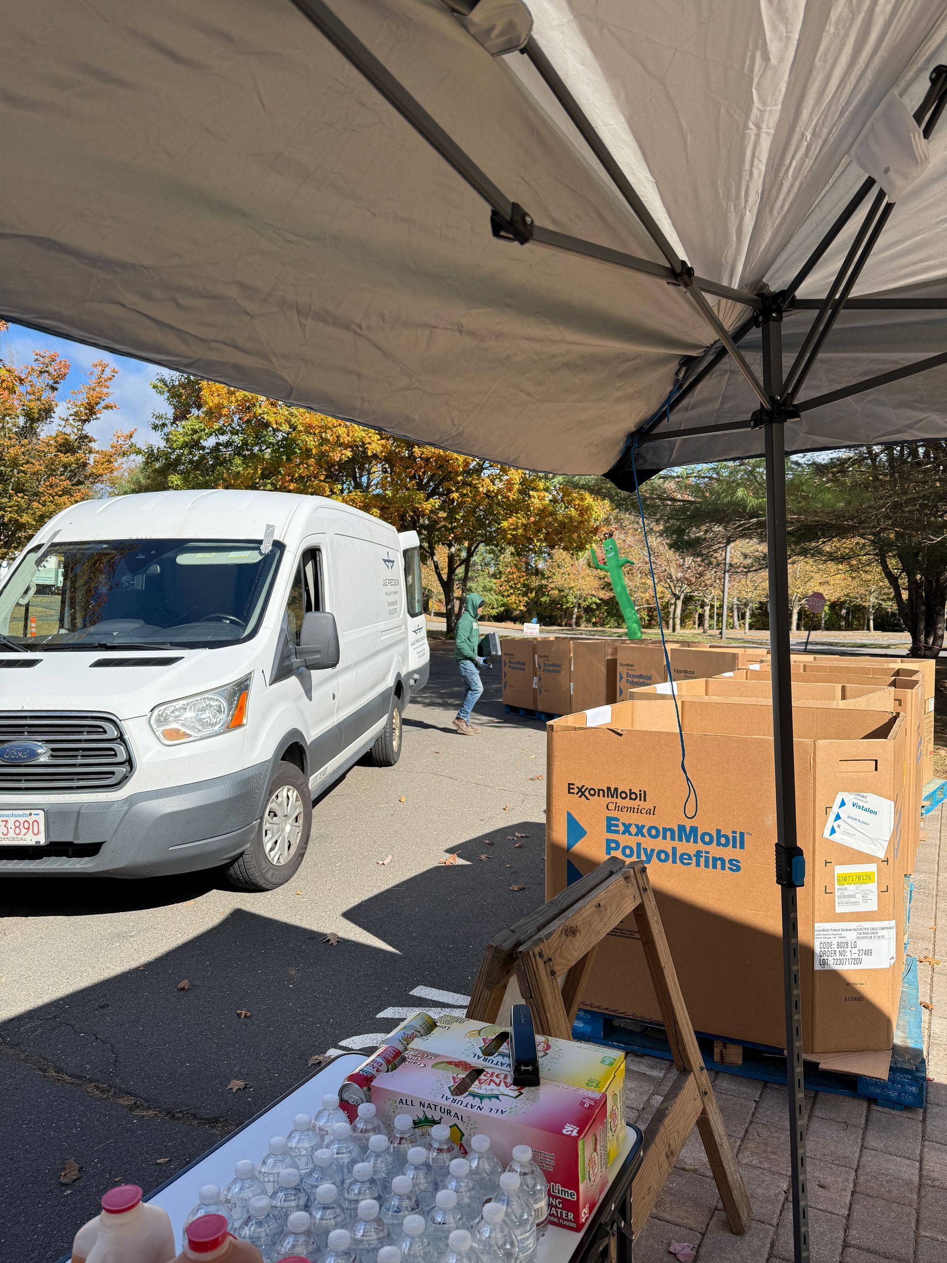 Volunteer table under a canopy beside a white van, with cardboard boxes and supplies outdoors.