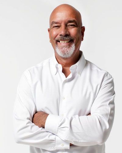 Smiling bald man in a white shirt, standing with arms crossed against a light background