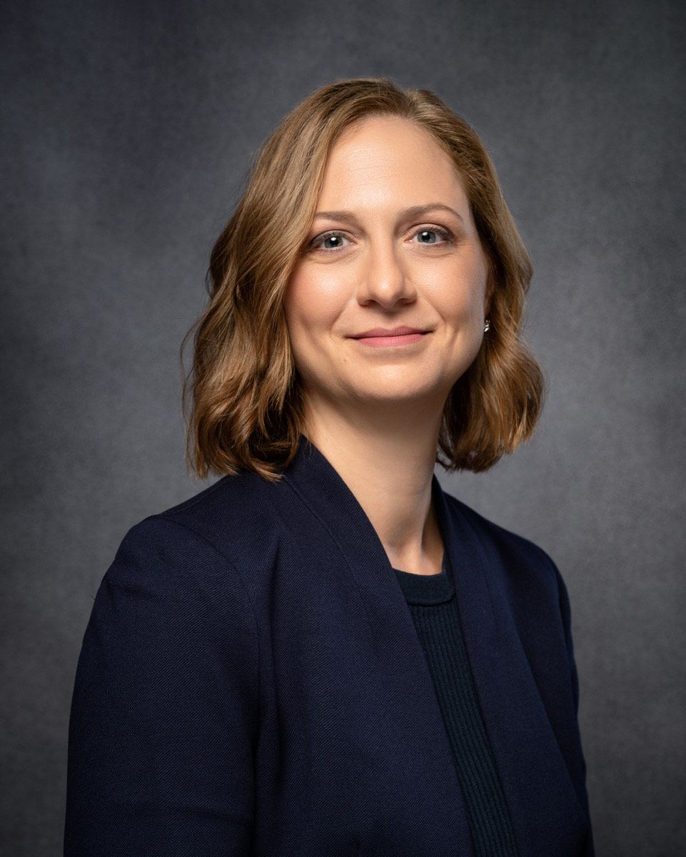 Portrait of a smiling person in a dark blazer against a gray studio backdrop