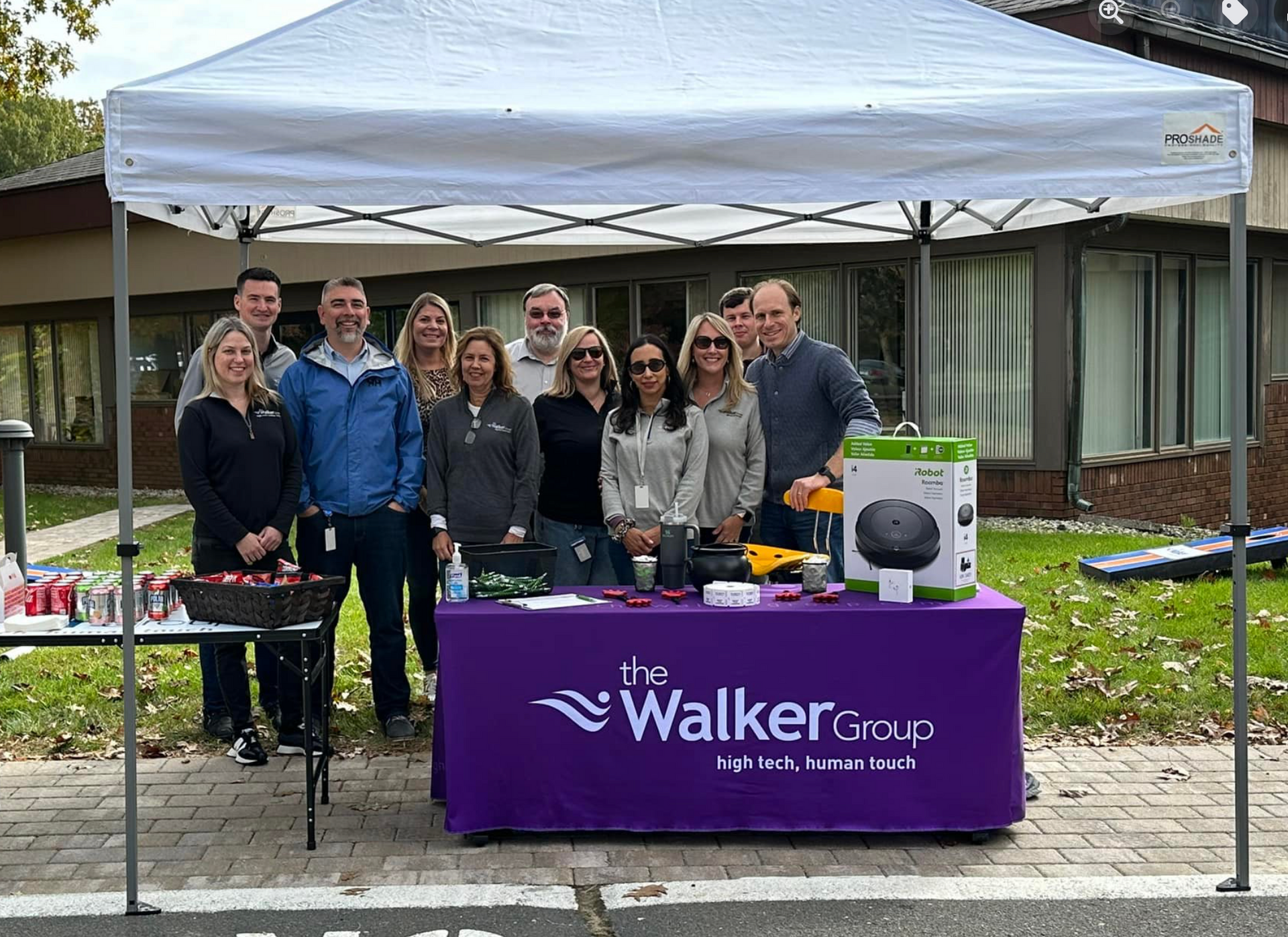 Group of people at an outdoor booth under a white canopy with a purple “Walker Cup” tablecloth.