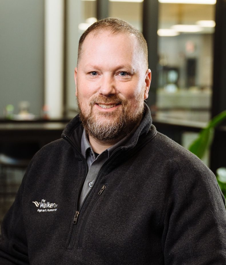 Smiling person in a black fleece jacket standing indoors in an office setting