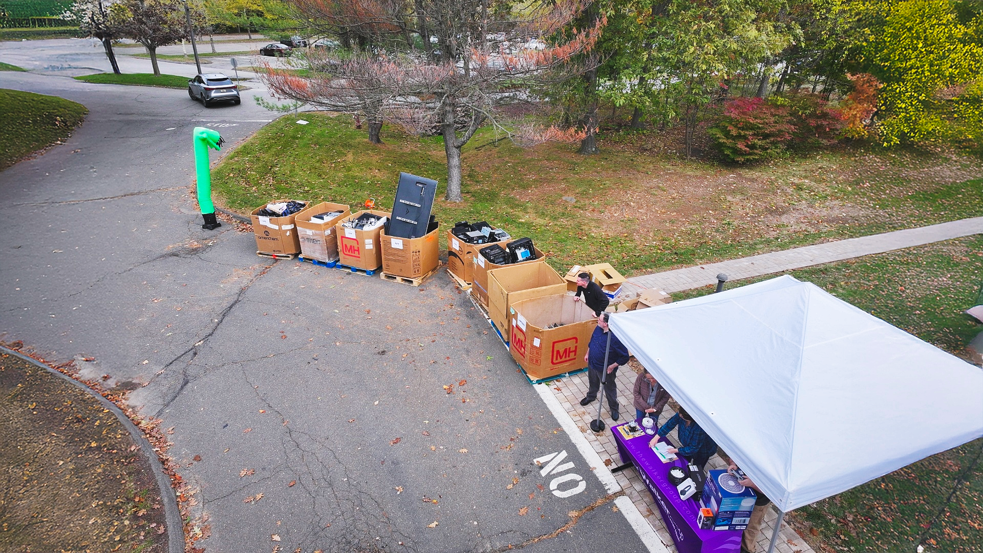 Donation boxes lined along a driveway beside a white canopy tent and green mailbox in a residential area