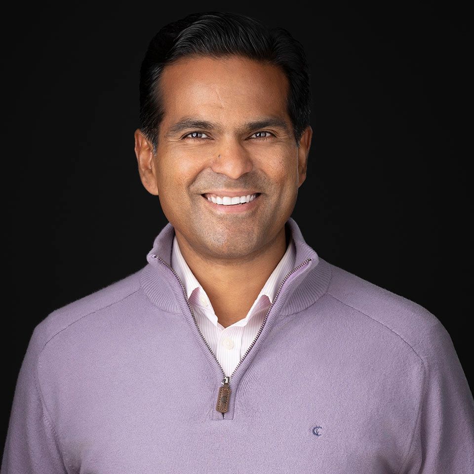 Smiling person in a light purple zip-up sweater against a dark background