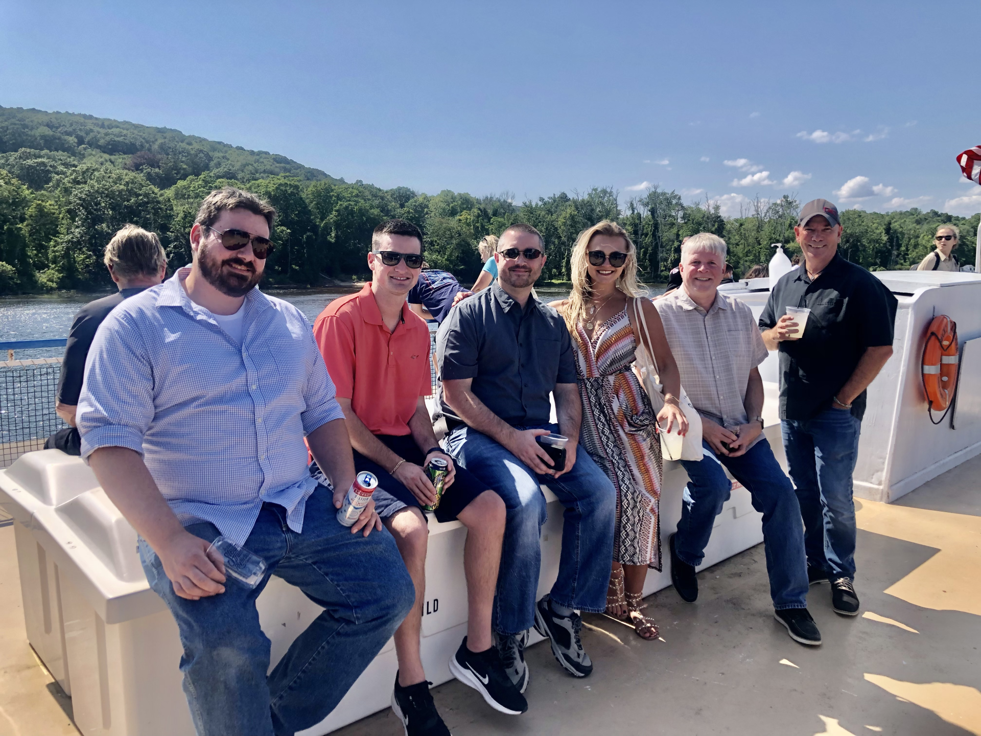 Six people seated on a boat deck with mountains and water in the background