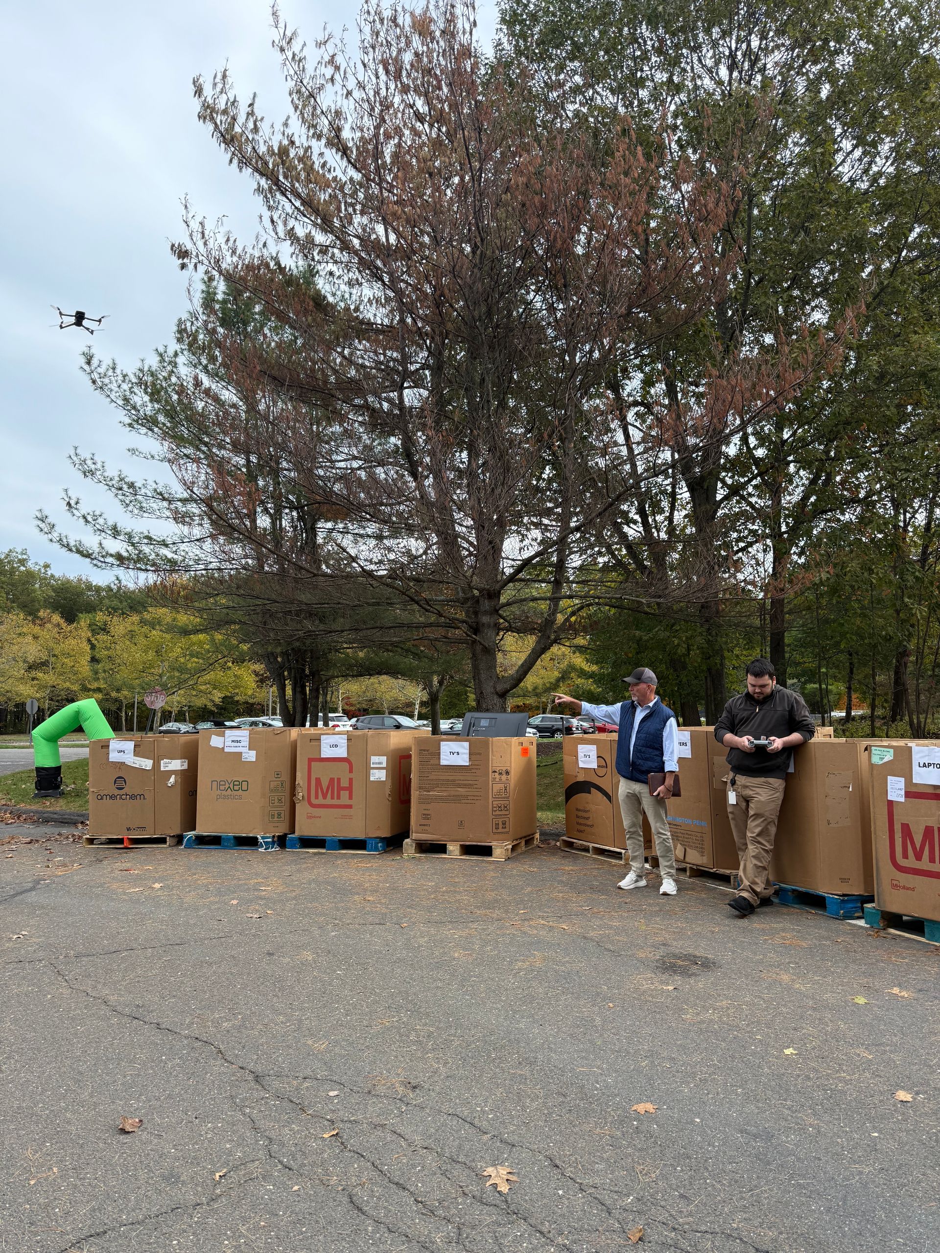 People lined up beside large cardboard donation boxes outdoors under trees.