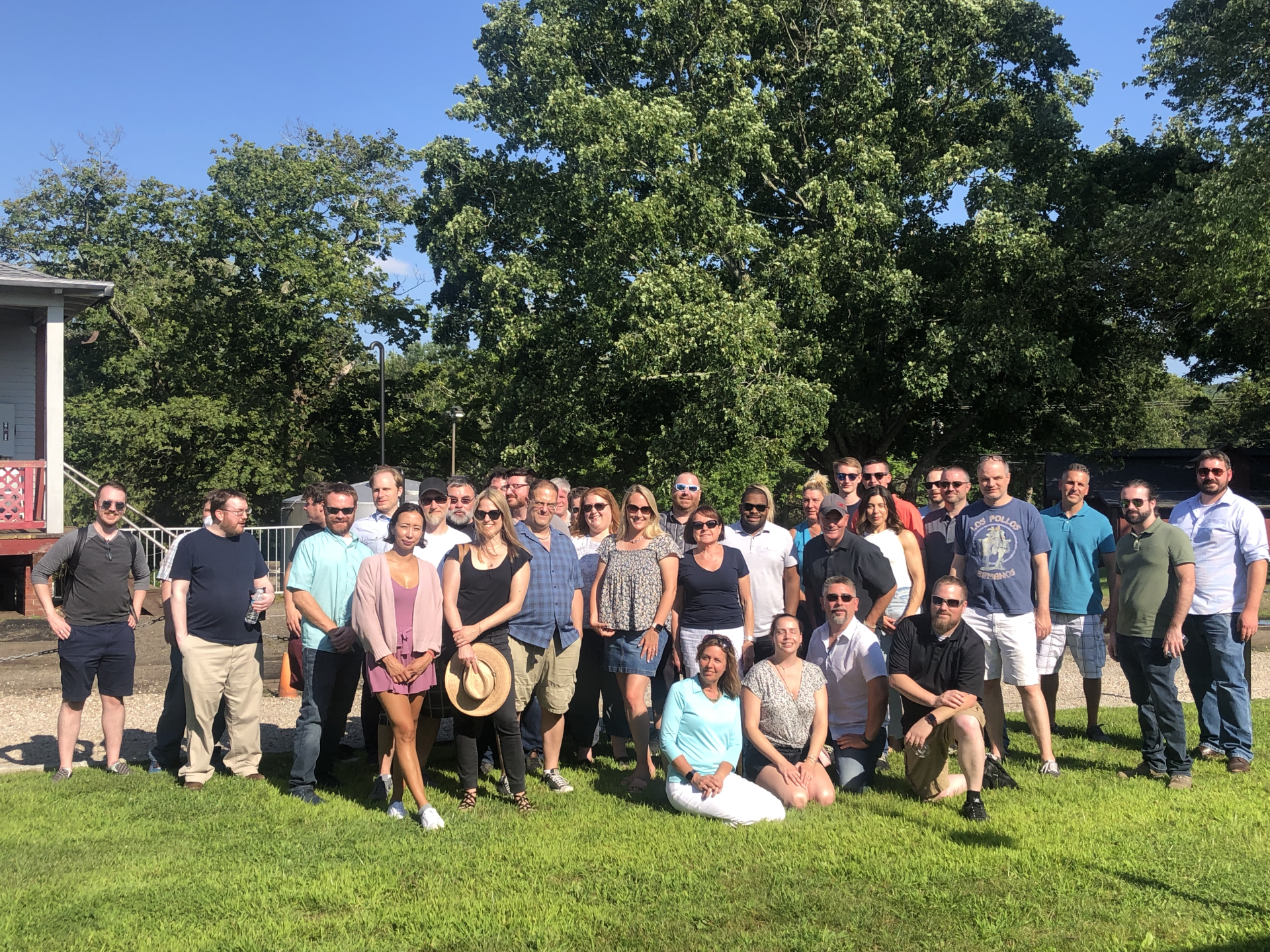 Group of people posing on a grassy lawn in front of trees on a sunny day