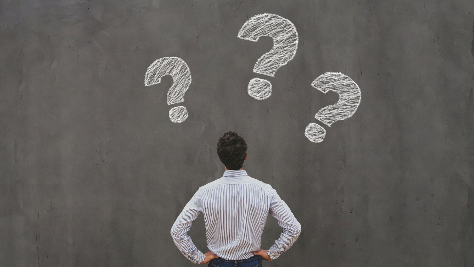 Man looking at a gray wall with three white question marks
