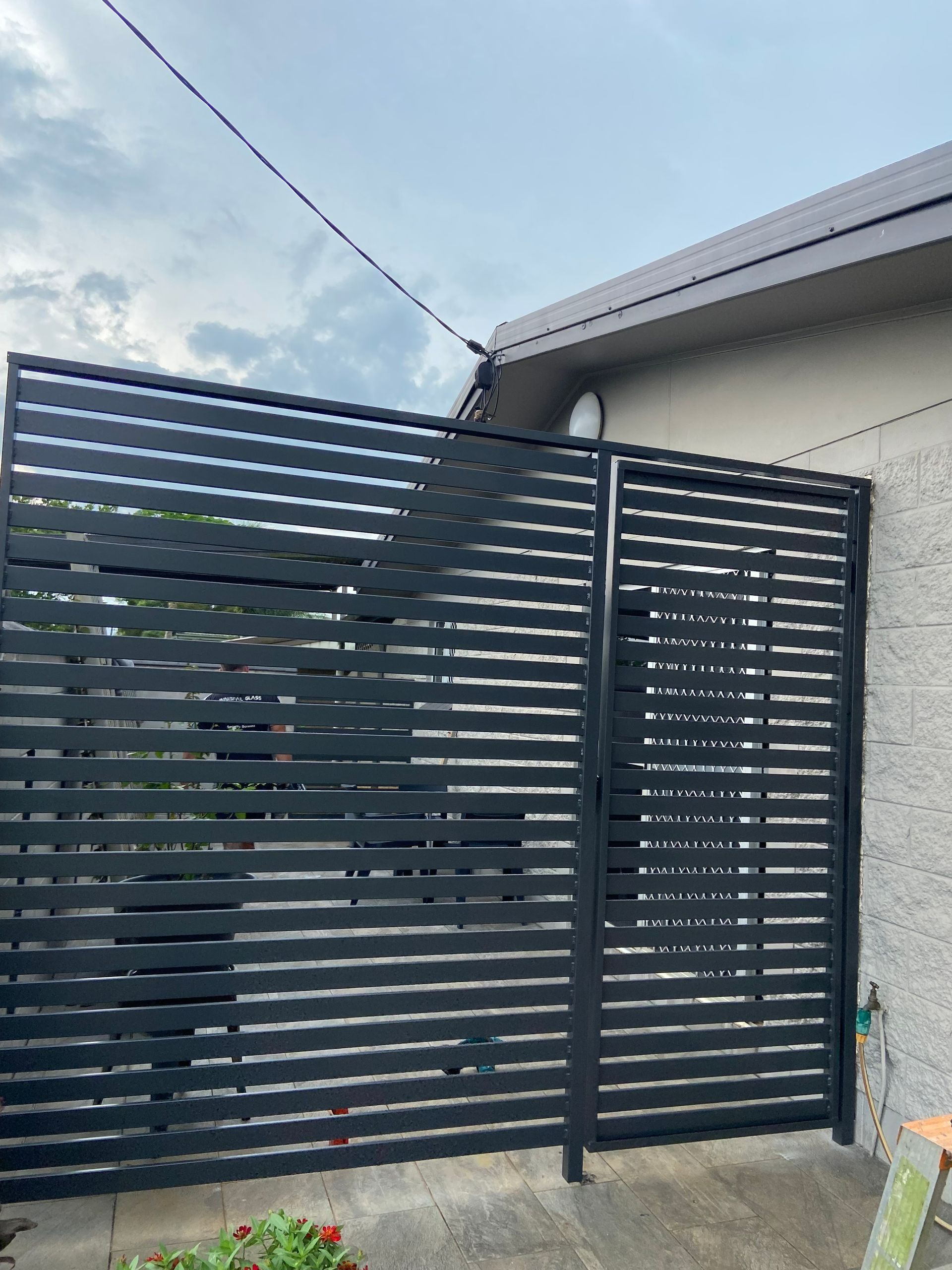 Black Horizontal Slat Gate Against a Beige Wall and Cloudy Sky — Innisfail Glass & Aluminium in Innisfail, QLD