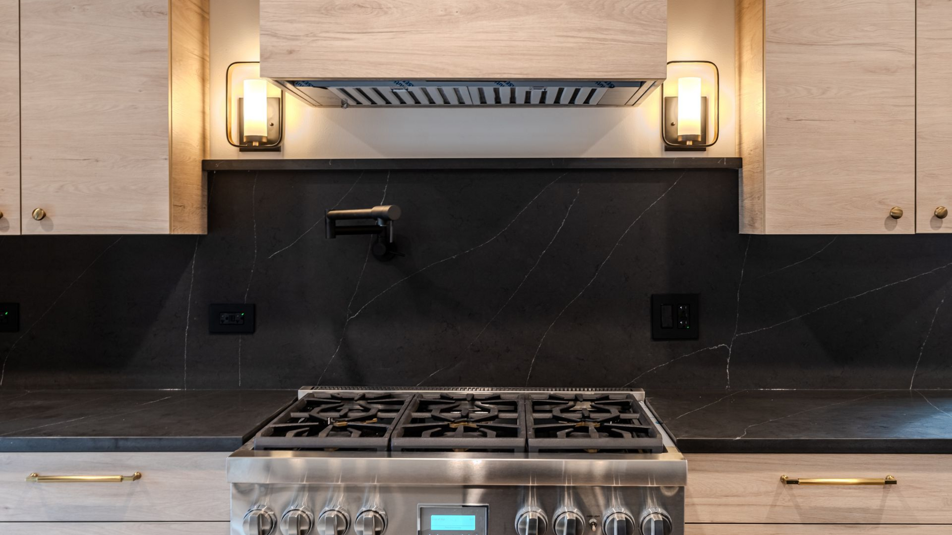 Modern kitchen with stainless steel stove, black backsplash, wood cabinets, and under-cabinet lights