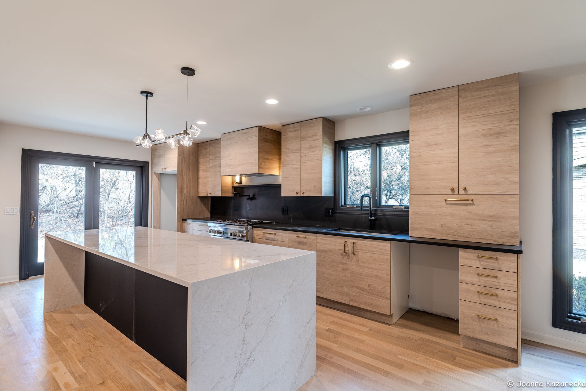 Modern kitchen with large marble island, wood cabinets, black backsplash, and bright natural light