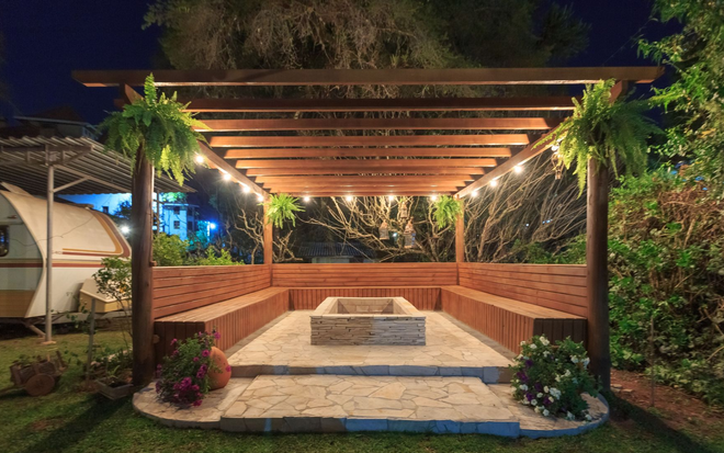 Outdoor brick seating area with wooden pergola, string lights, and central fire pit at night