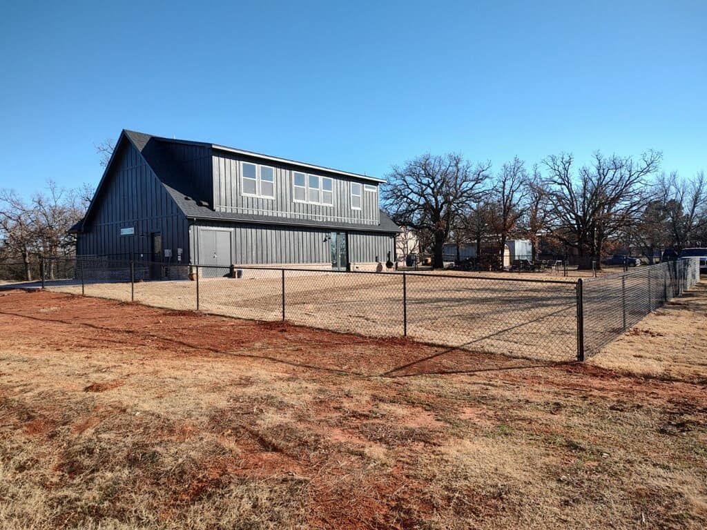 A large barn is sitting in the middle of a field next to a fence.