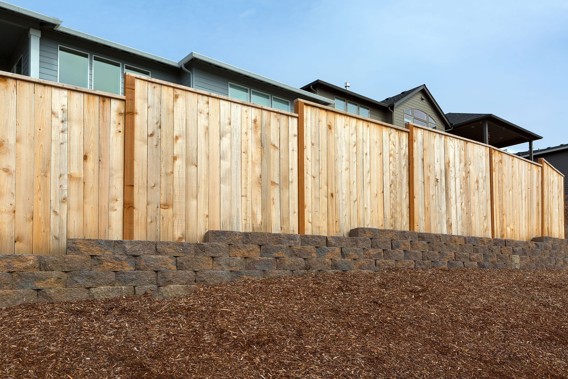 Wood privacy fence on a stone retaining wall in front of homes.