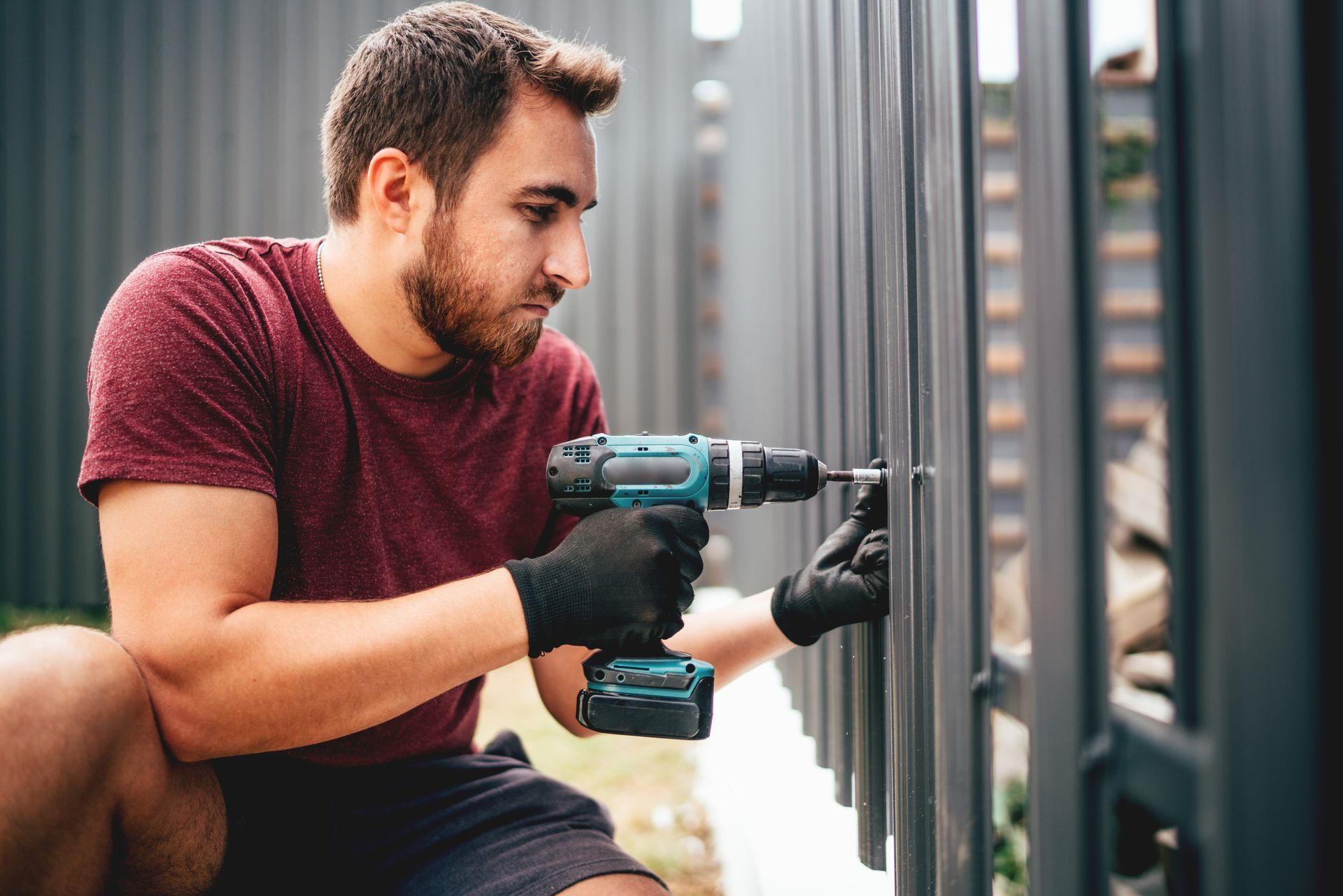 Person using a power drill to fasten screws onto a metal fence panel outdoors.