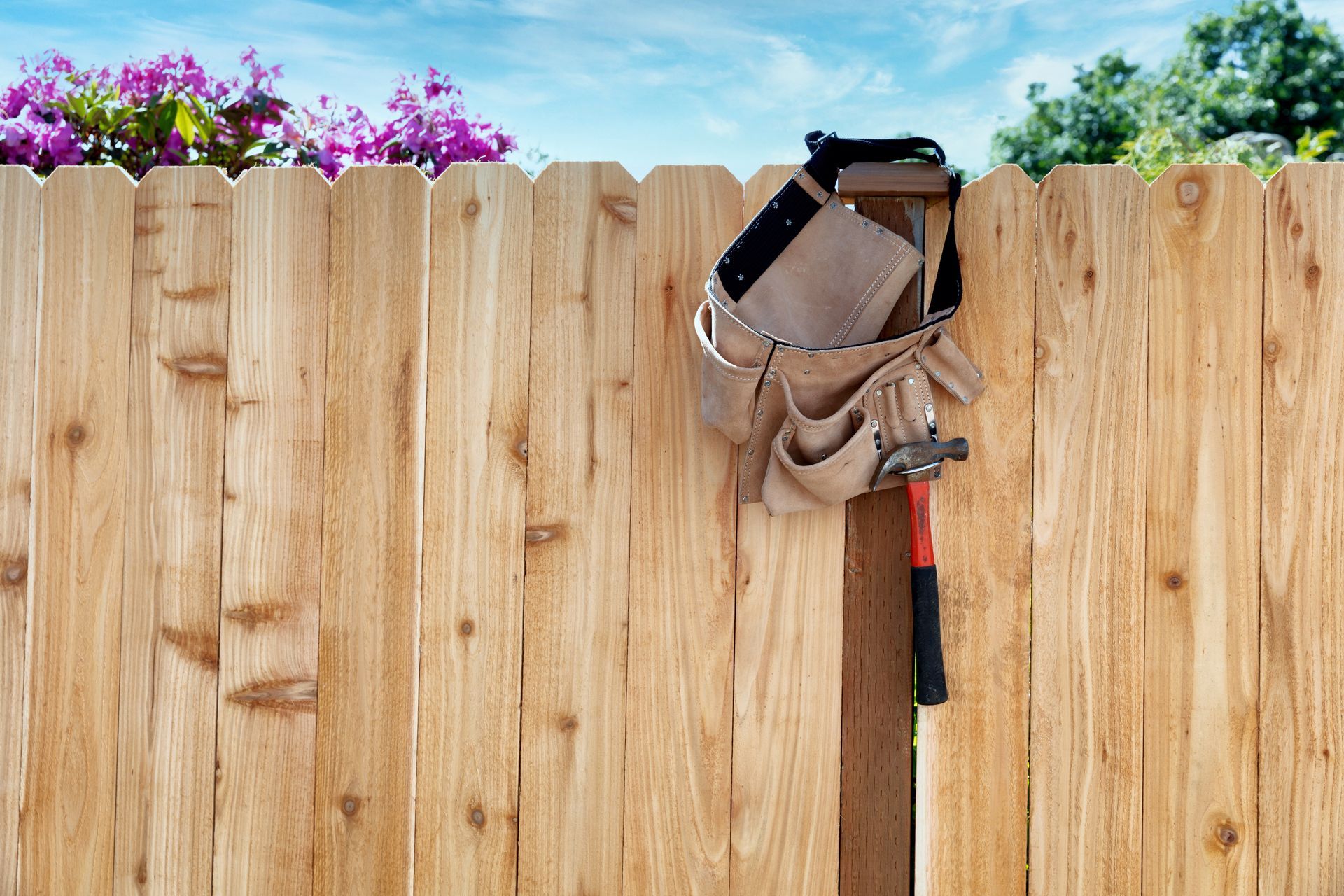 Wooden privacy fence with tool belt and hammer hanging on it.