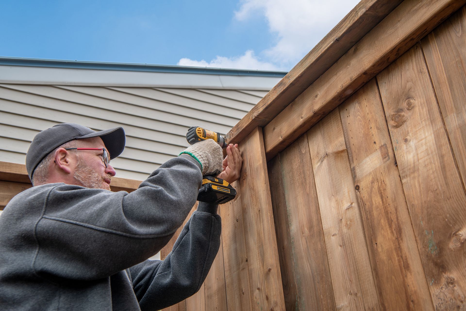 Man using a power drill to secure wooden fence boards outdoors.