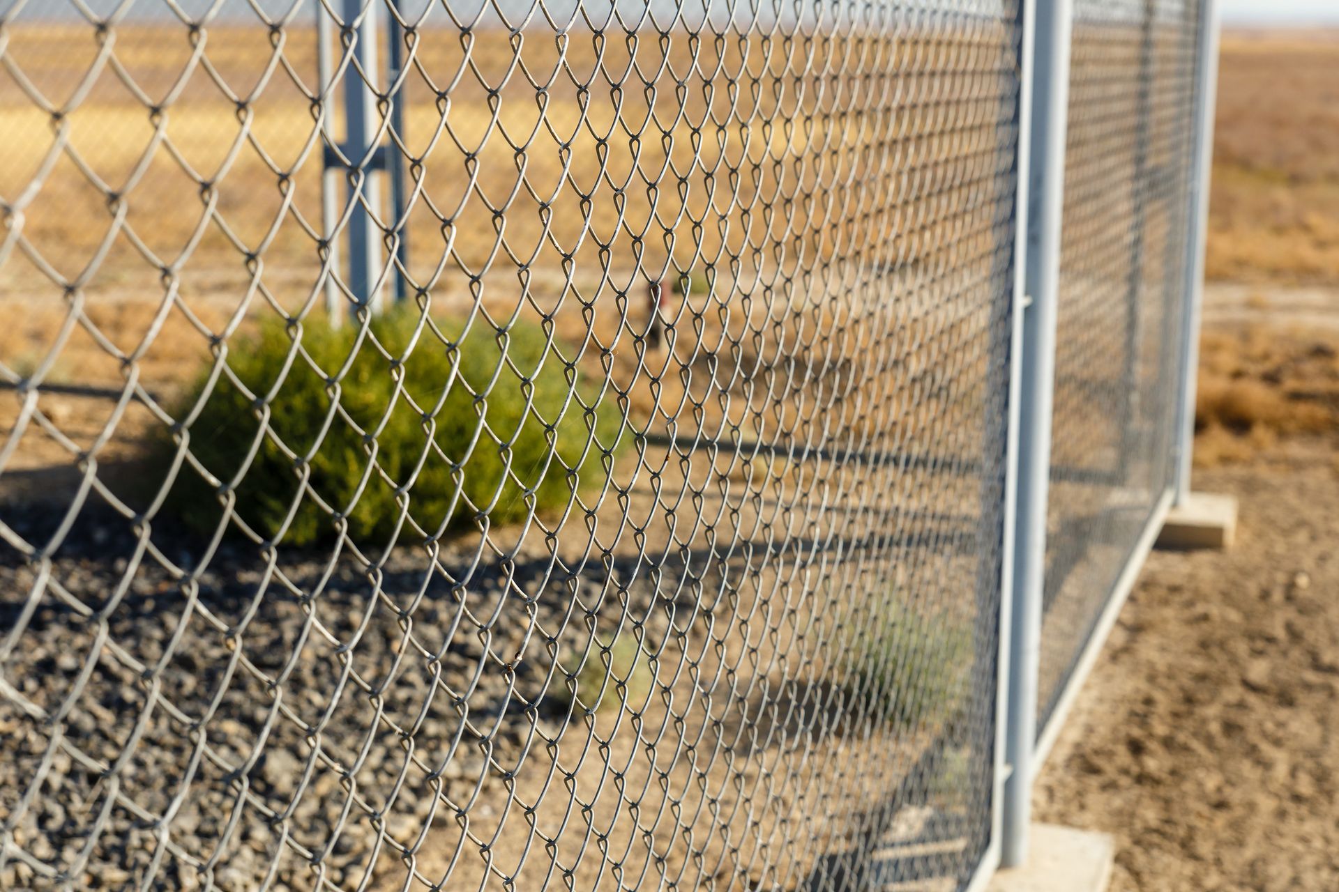 A chain link fence is surrounding a field in the desert.