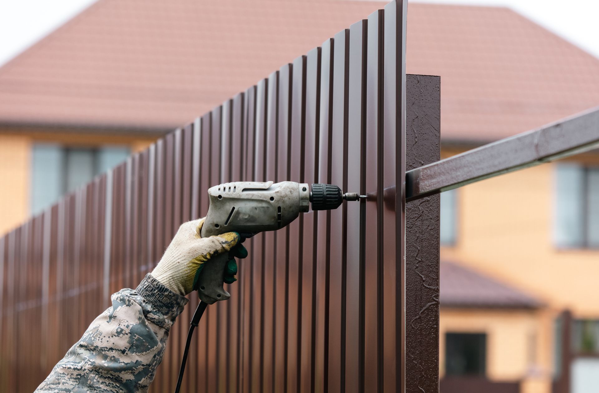 Person using a power drill to install a metal fence panel.